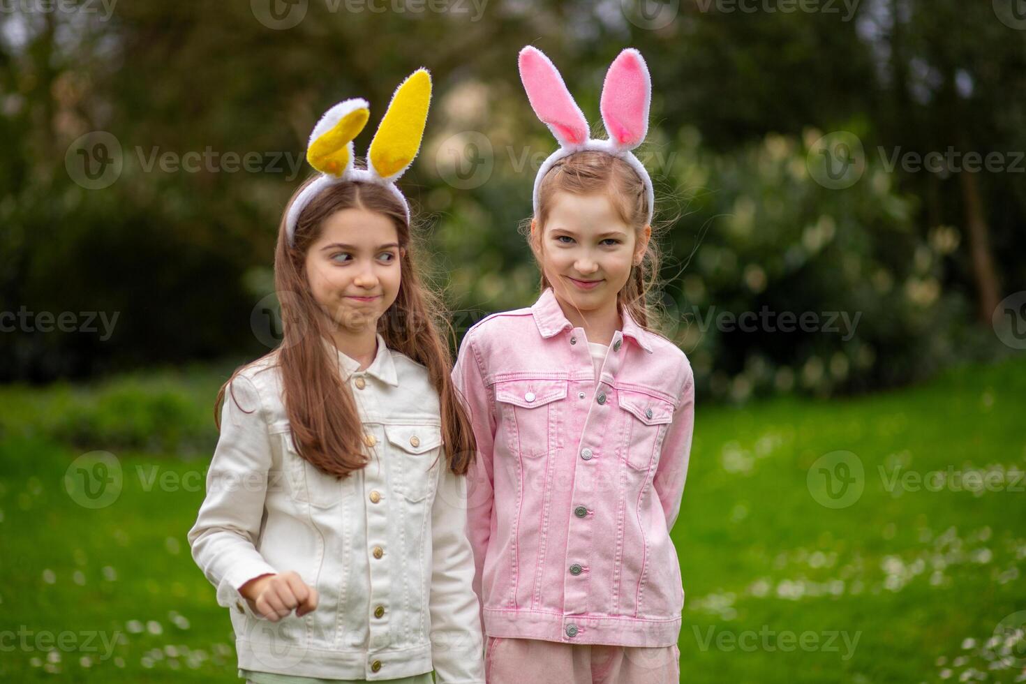 Two children wearing bunny ears in a sunny park enjoying Easter festivities while posing together photo