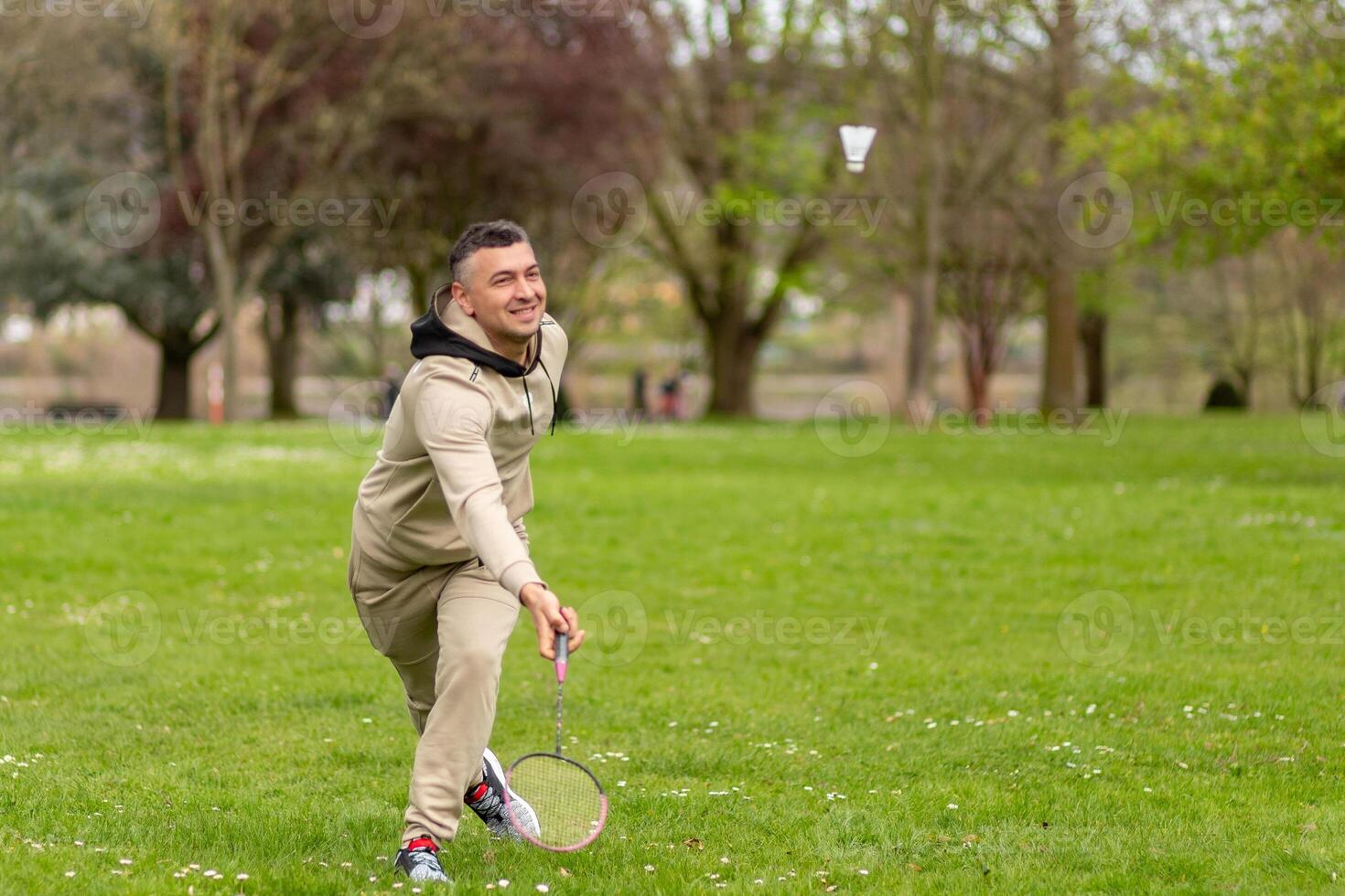 A man in a beige tracksuit plays badminton in the park photo