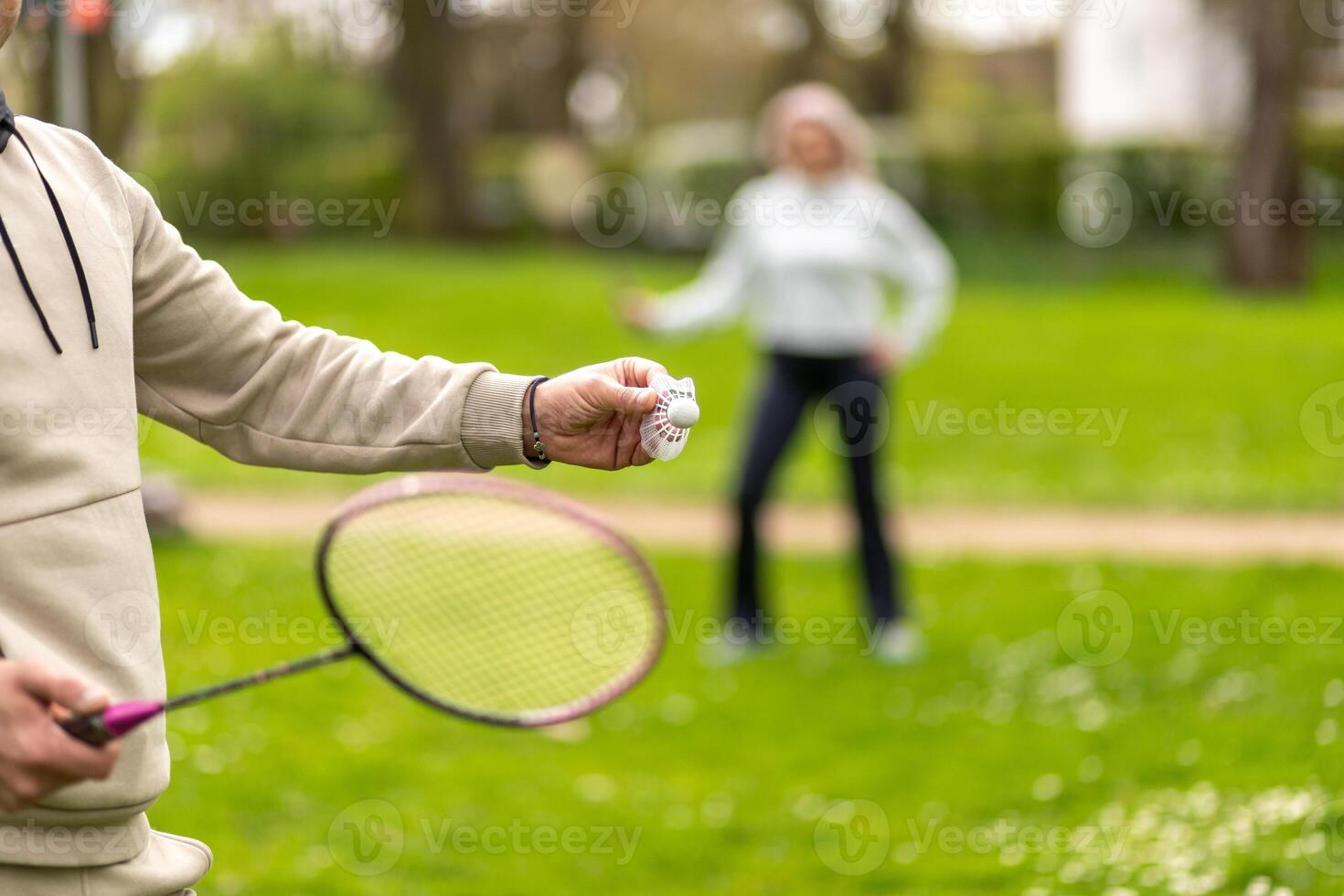 Man and woman playing badminton outdoors, focus on hand with shuttlecock photo