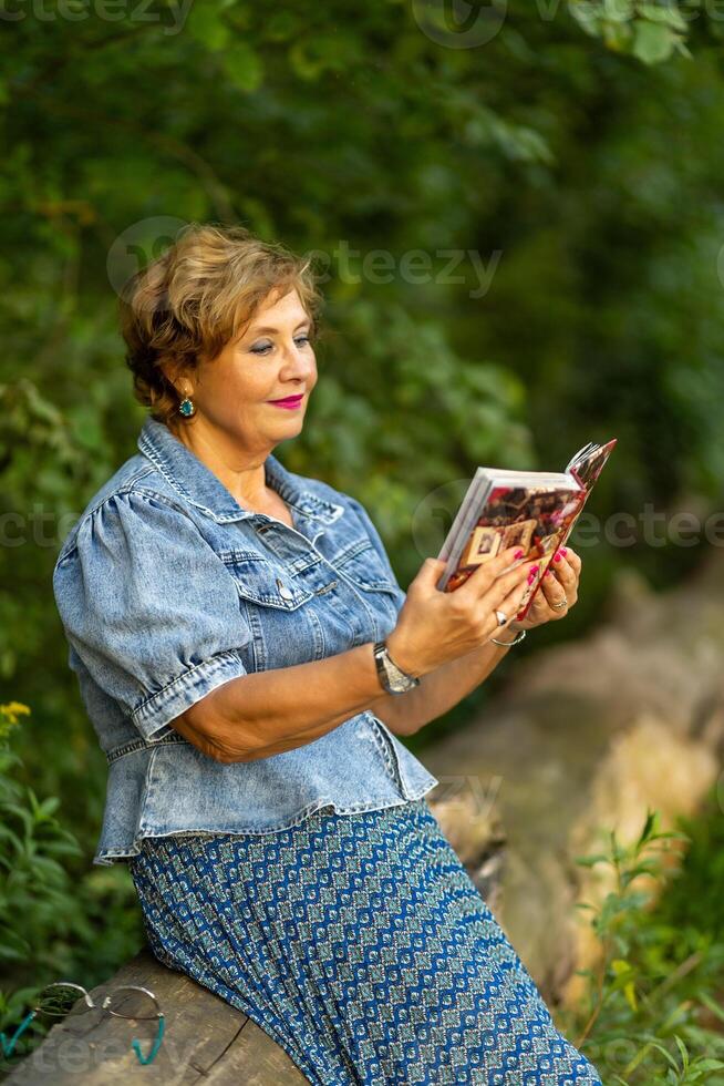 Woman reading a book while sitting on a log in a lush green forest photo