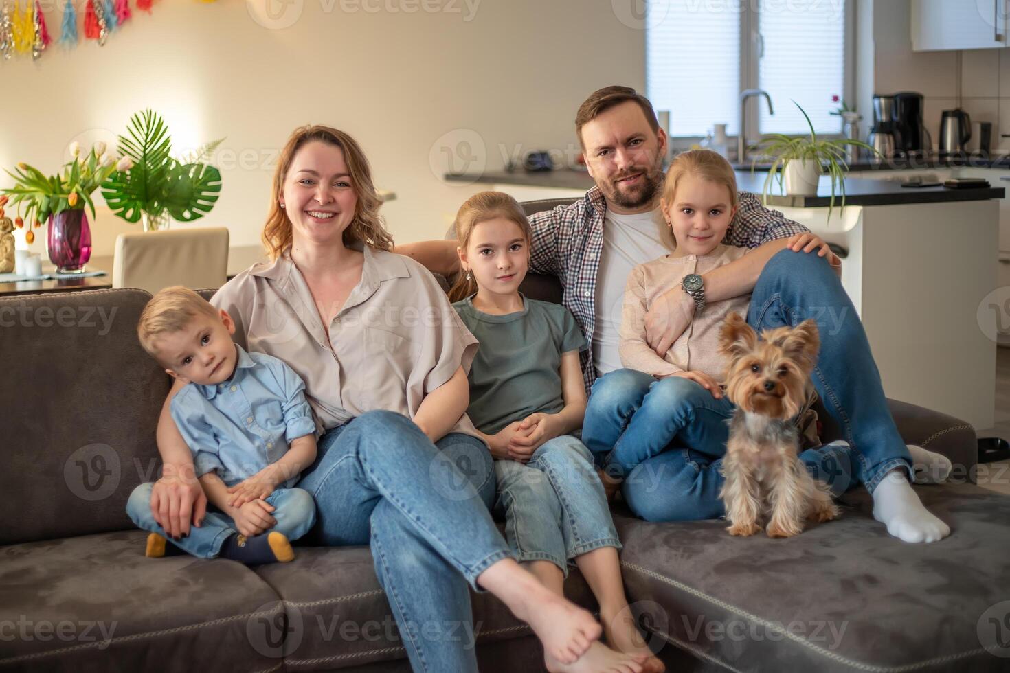 family portrait. family photo in which mom, dad, daughters, son and dog are smiling and hugging on the couch in a cozy homely atmosphere