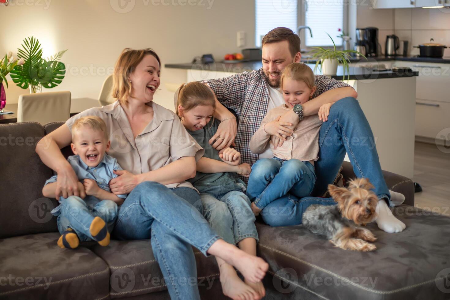 family portrait. family photo in which mom, dad, daughters, son and dog are smiling and hugging on the couch in a cozy homely atmosphere