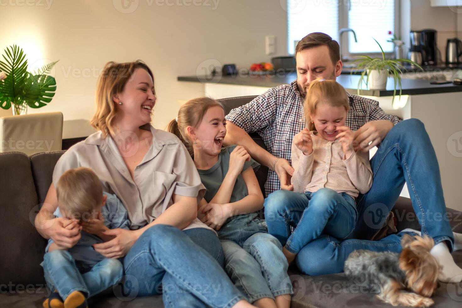 family portrait. family photo in which mom, dad, daughters, son and dog are smiling and hugging on the couch in a cozy homely atmosphere