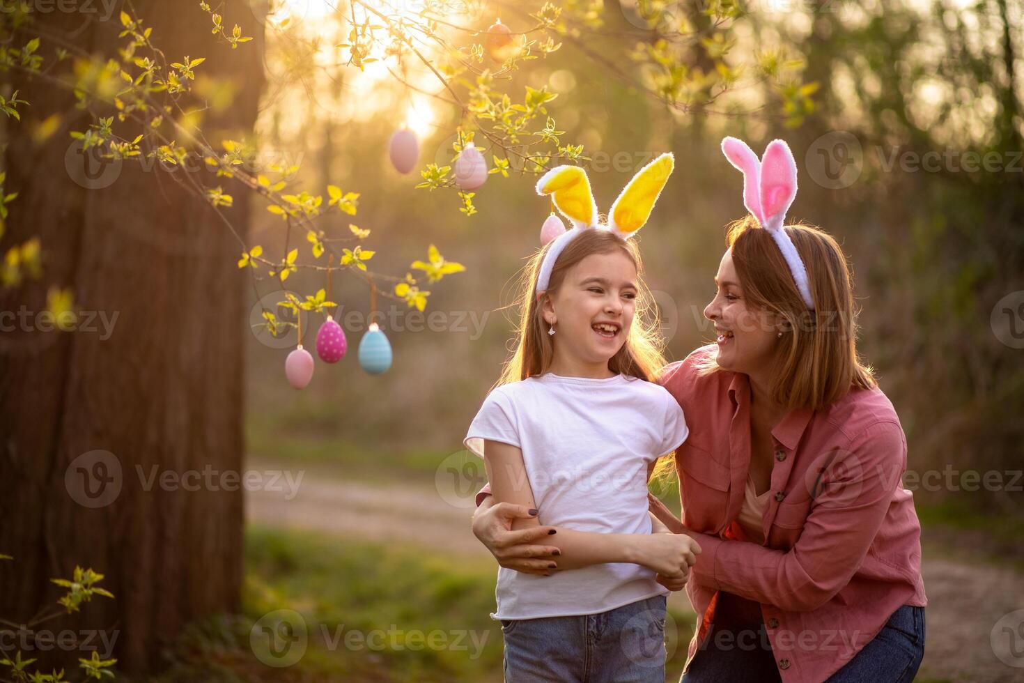 beautiful and happy mom and daughter in bunny ears decorate the tree with easter eggs. happy family celebrating easter photo