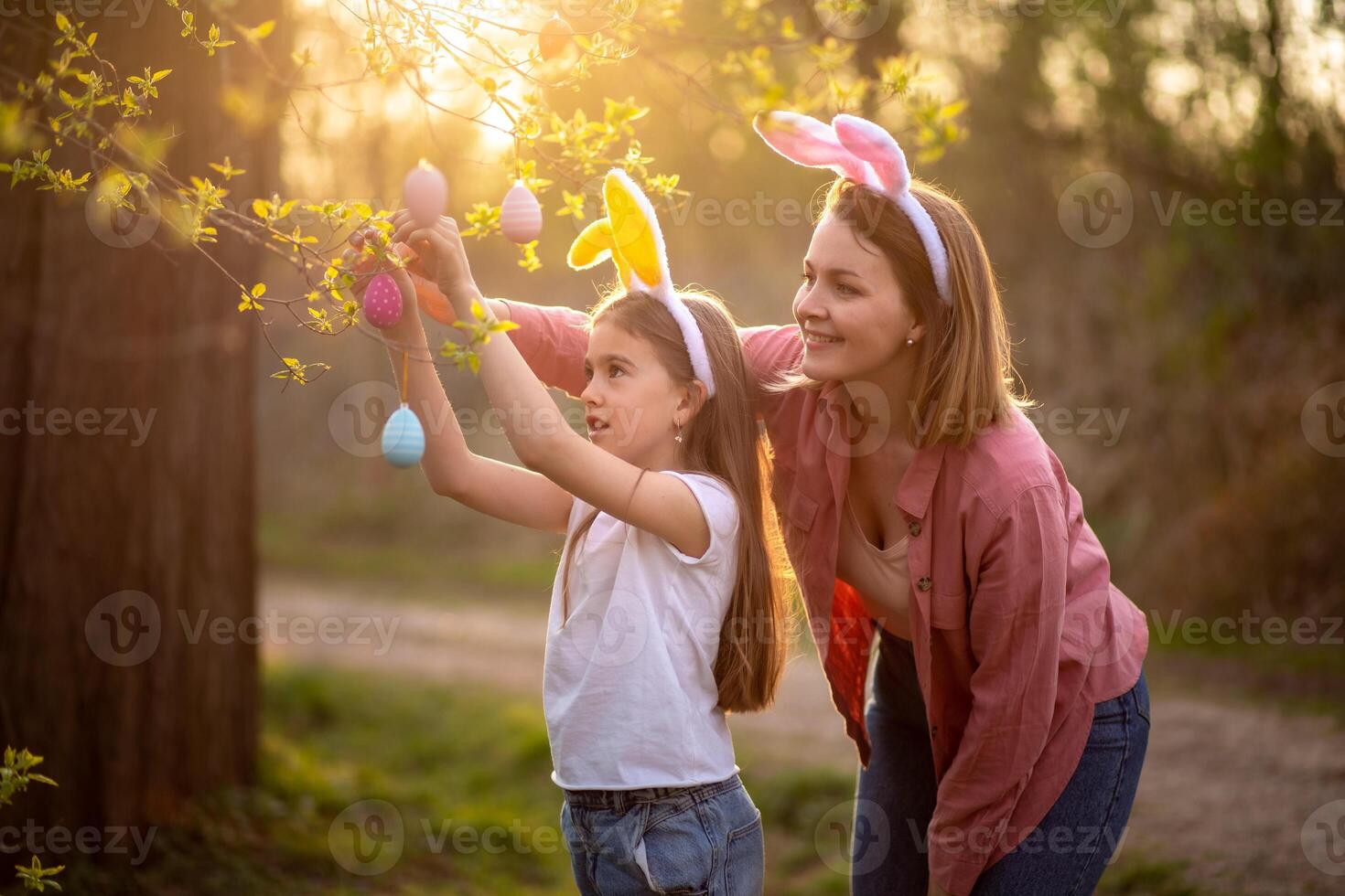 beautiful and happy mom and daughter in bunny ears decorate the tree with easter eggs. happy family celebrating easter photo