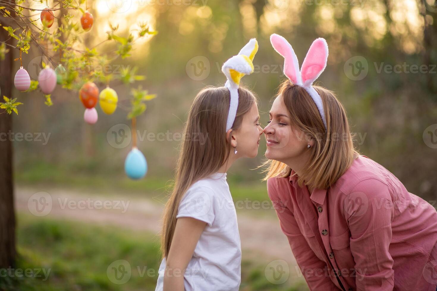 beautiful and happy mom and daughter in bunny ears decorate the tree with easter eggs. happy family celebrating easter photo