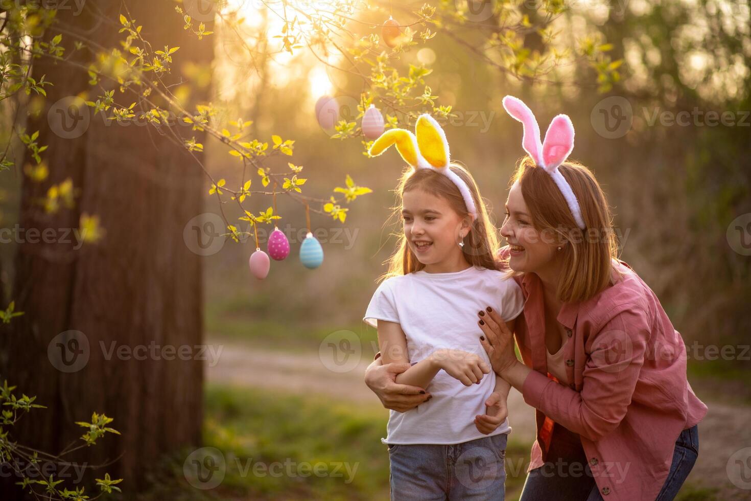 beautiful and happy mom and daughter in bunny ears decorate the tree with easter eggs. happy family celebrating easter photo