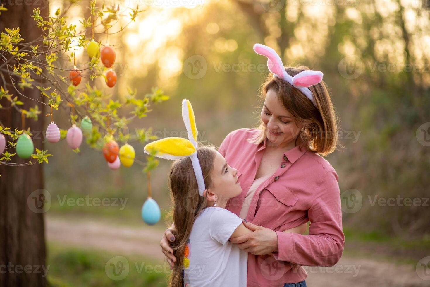 beautiful and happy mom and daughter in bunny ears decorate the tree with easter eggs. happy family celebrating easter photo