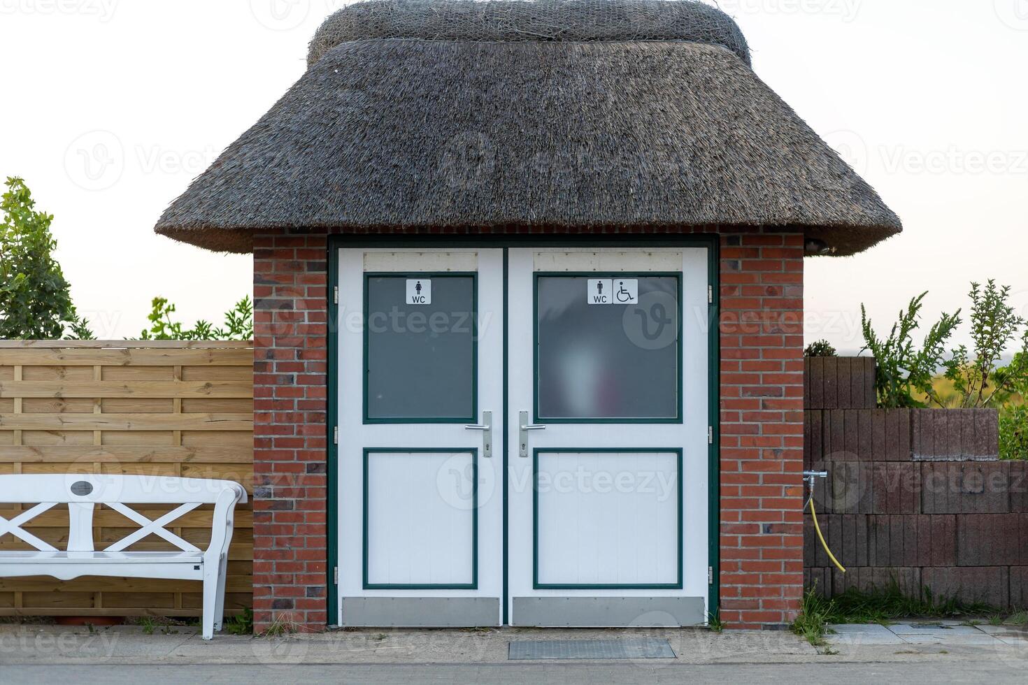 Unique thatched roof public restroom facility near a park, with clean doors and seating available outside for visitors photo