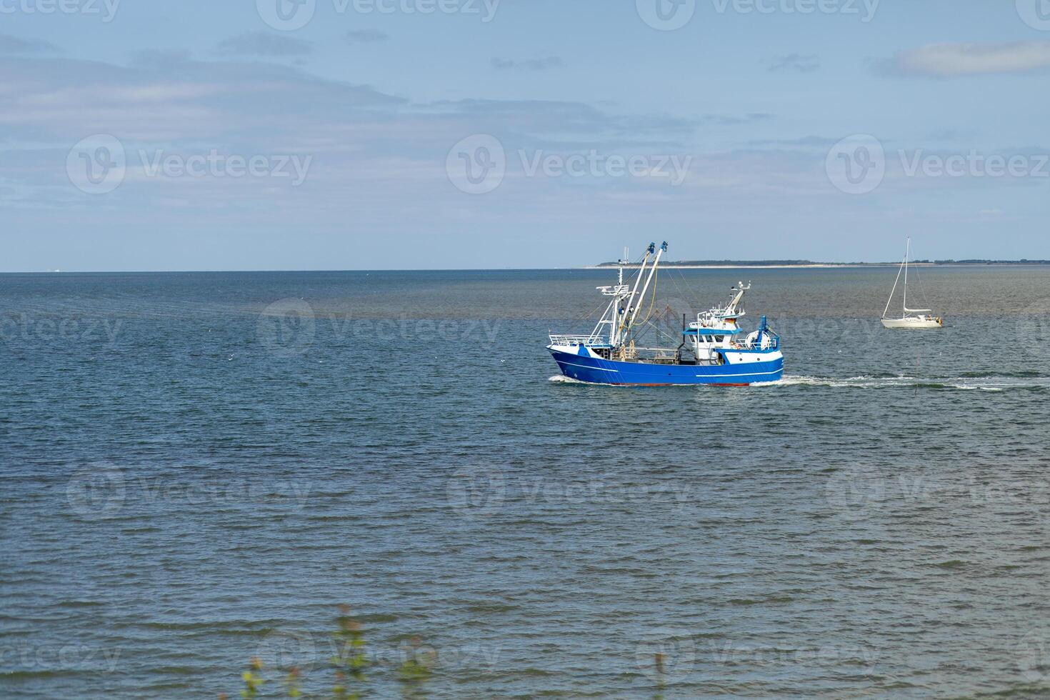 A fishing boat navigates the calm waters near the shore, with a sailboat in the background on a clear sunny day photo