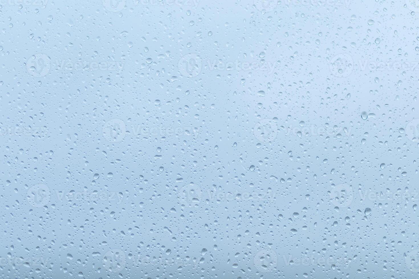 Raindrops collecting on a window during a gloomy day, creating a blurred view of the overcast sky outside photo
