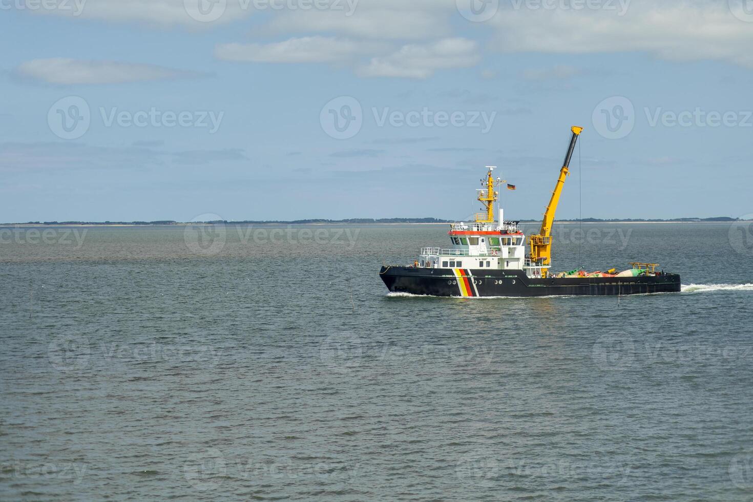 A utility vessel navigates smooth waters near a coastal region on a clear day, showcasing efficient marine operation and maintenance activities photo