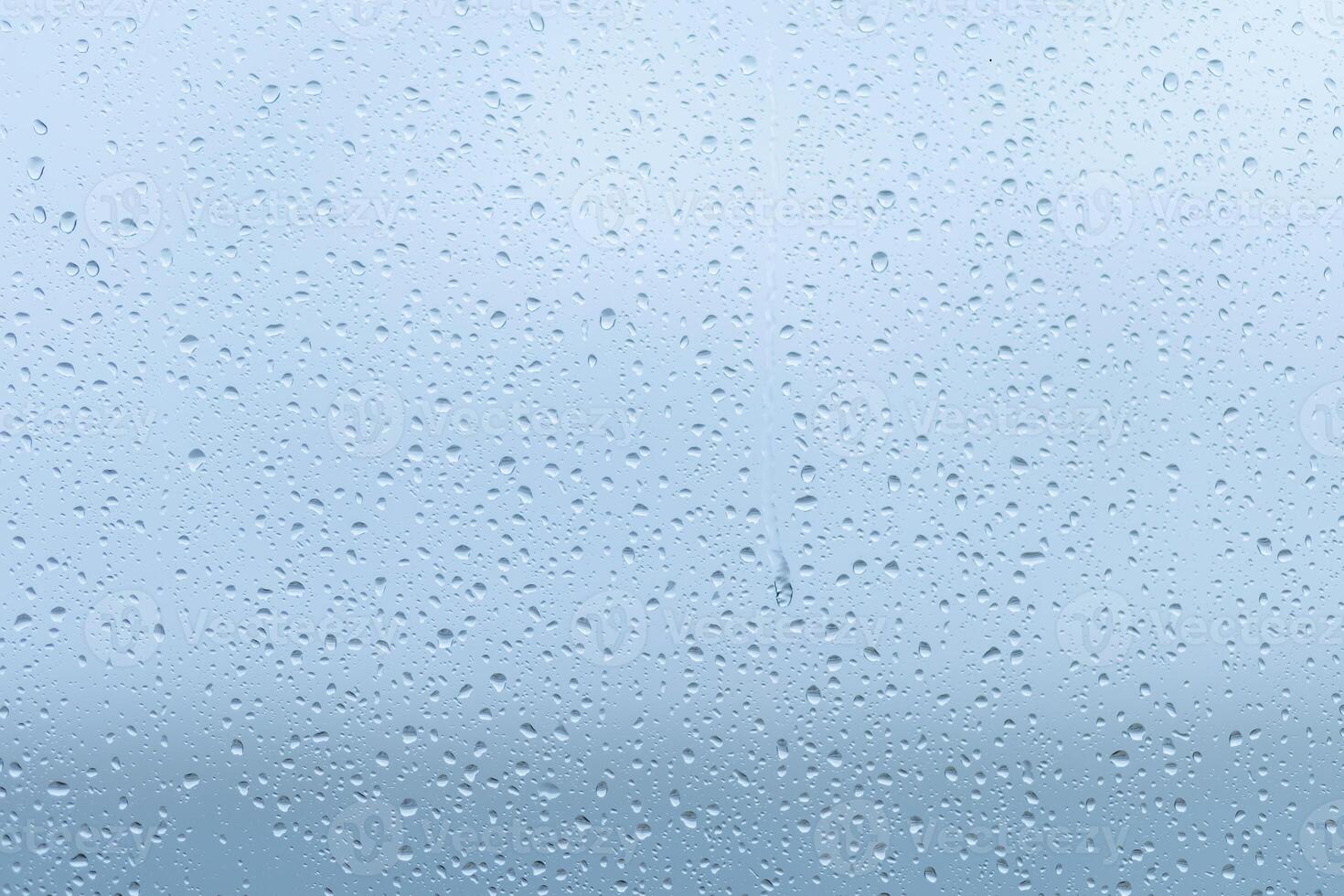 Raindrops forming a delicate pattern on a window pane, blurring the outside view during a cloudy afternoon in early fall photo