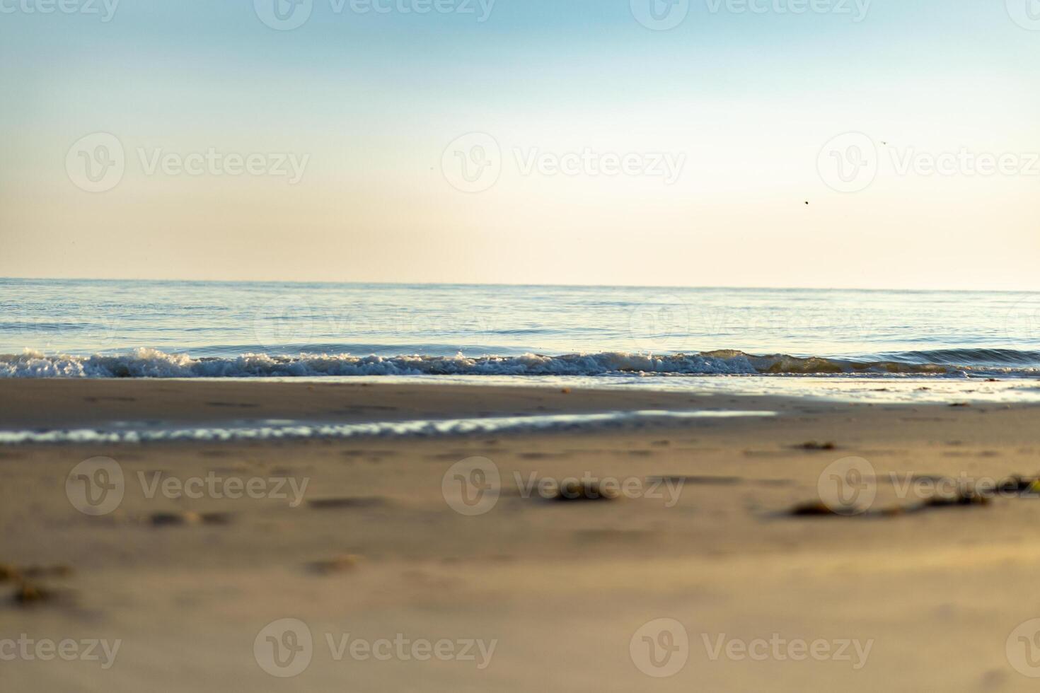 Waves gently lap on the sandy shore under a clear sky during the early evening at a tranquil beach photo