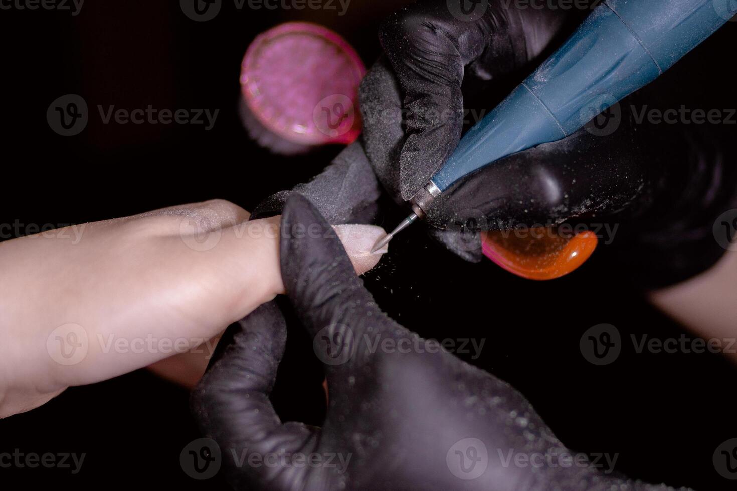 Technician in black gloves using electric tool to polish client's nail. photo