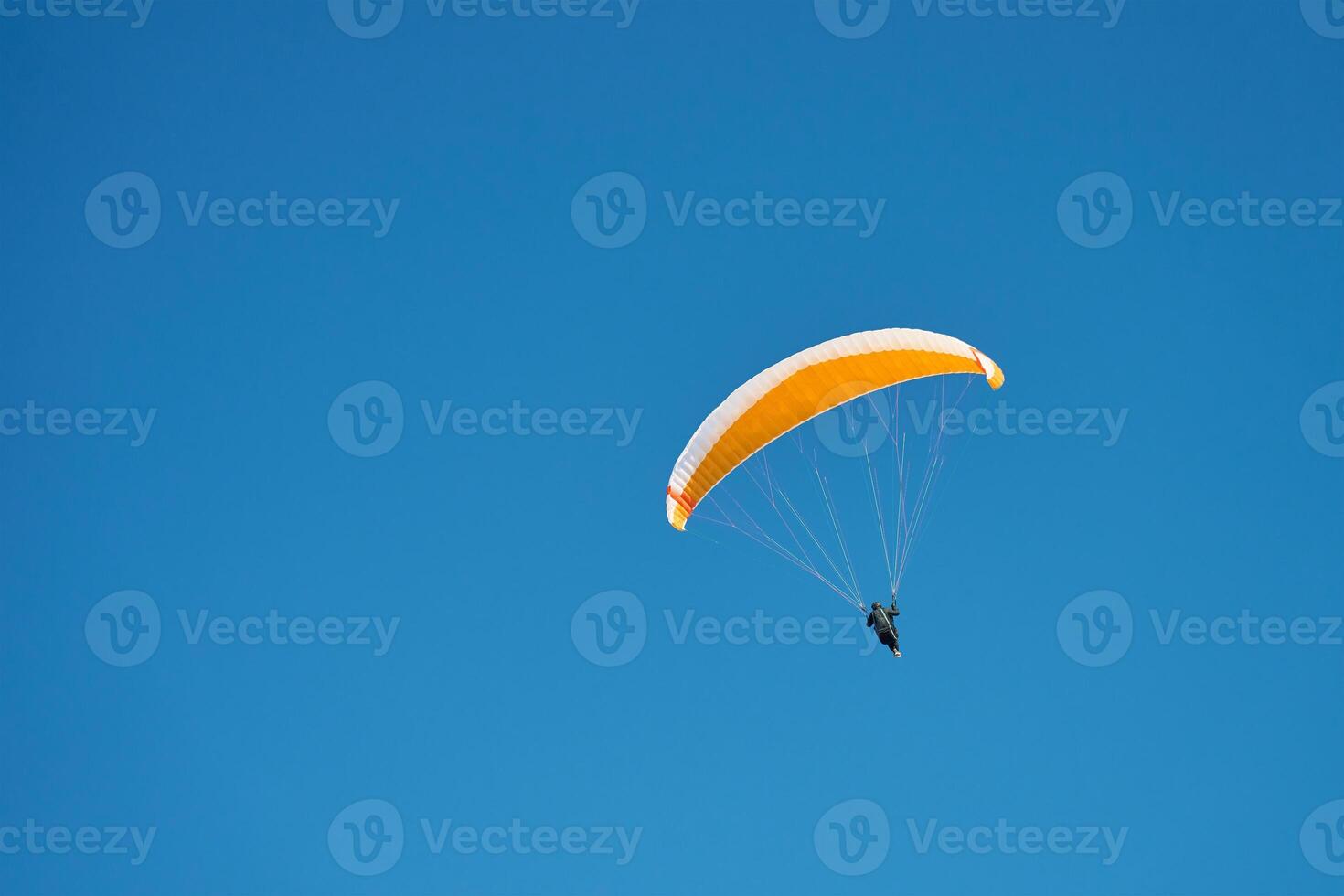 Person is flying on paraglider against blue sky. Paraglide with yellow canopy. Extremal sport photo