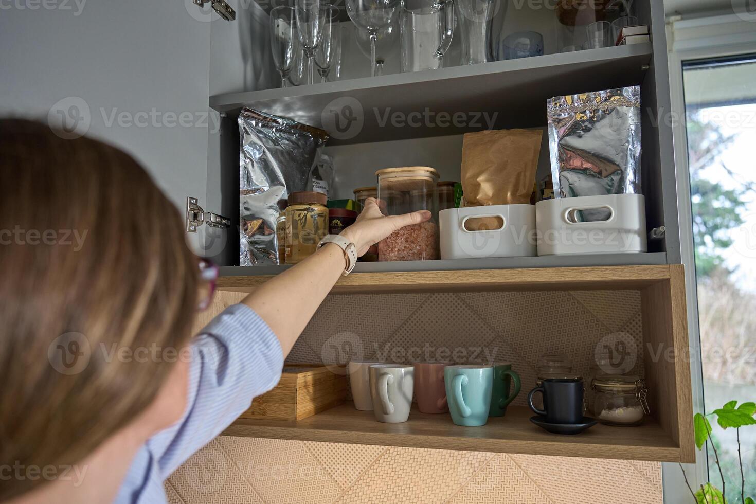 Woman taking jar in kitchen cabinet with stored cooking ingredients photo