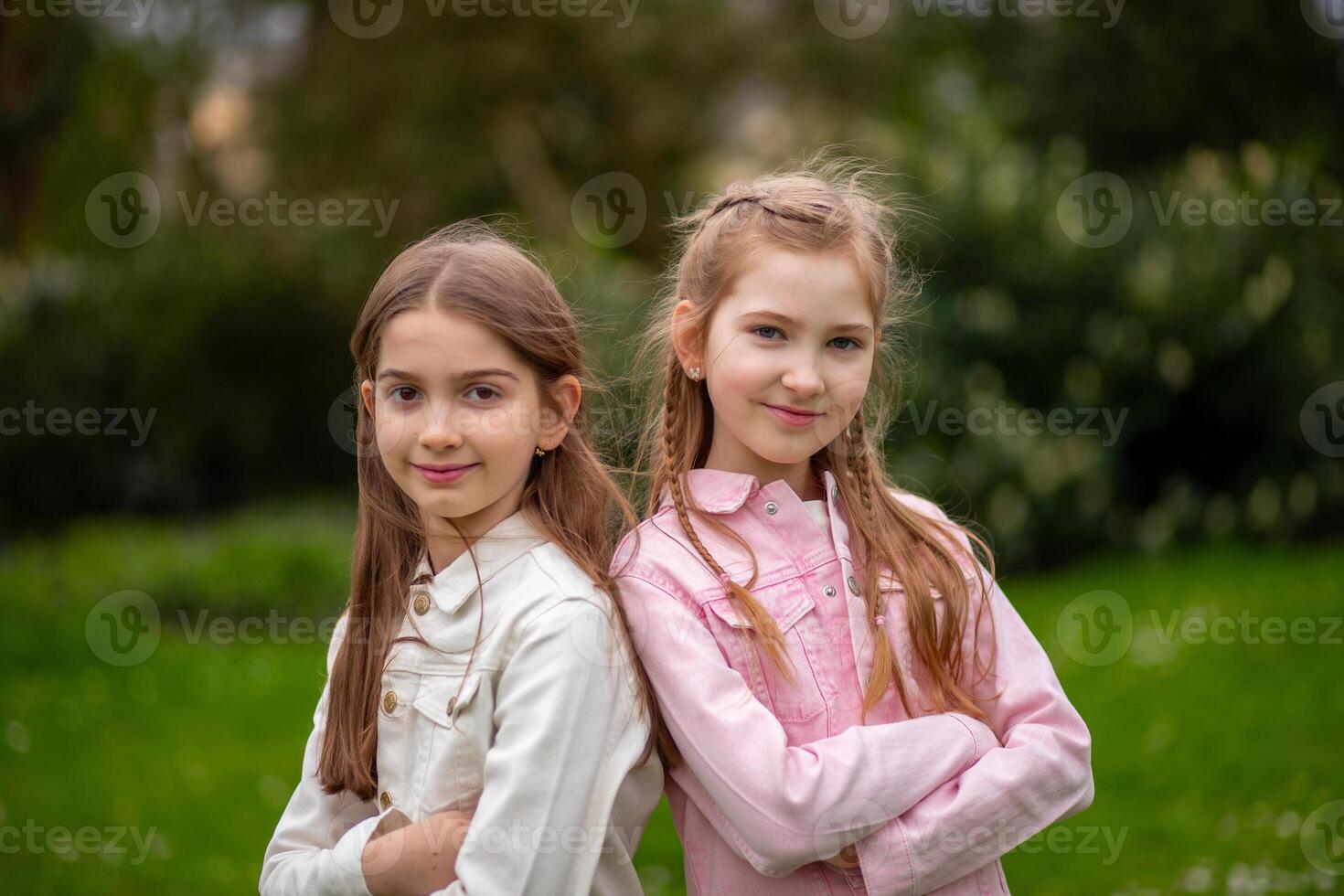 Two charming girls in pastel-shaded outfits, smiling amiably and posing in a green spring park. photo