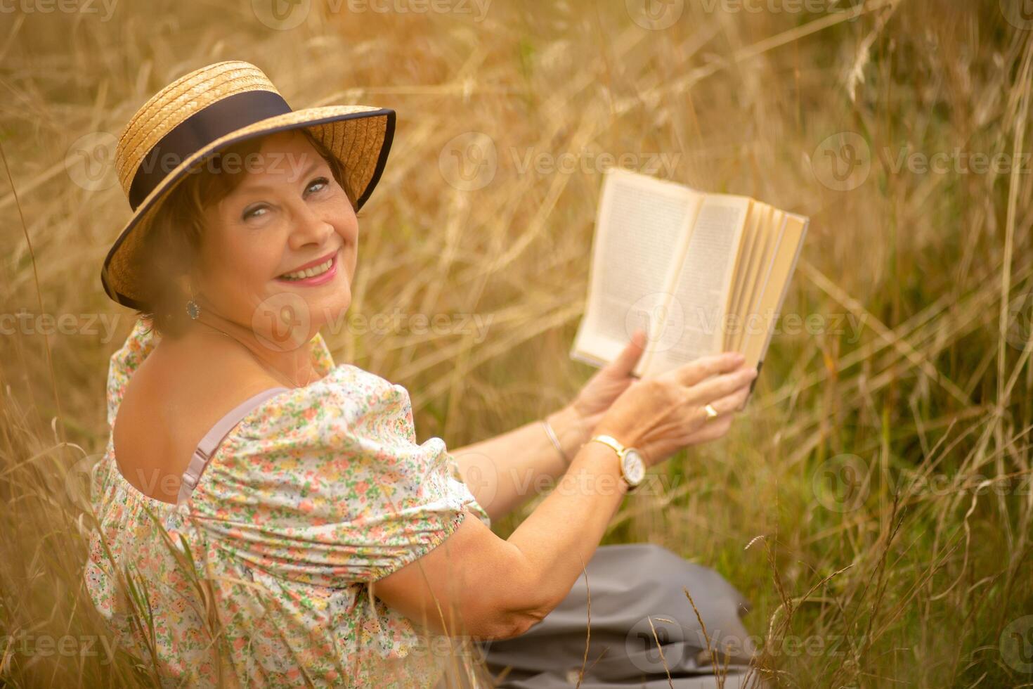 A woman enjoying a book in a sunny field during summer, surrounded by tall grass photo