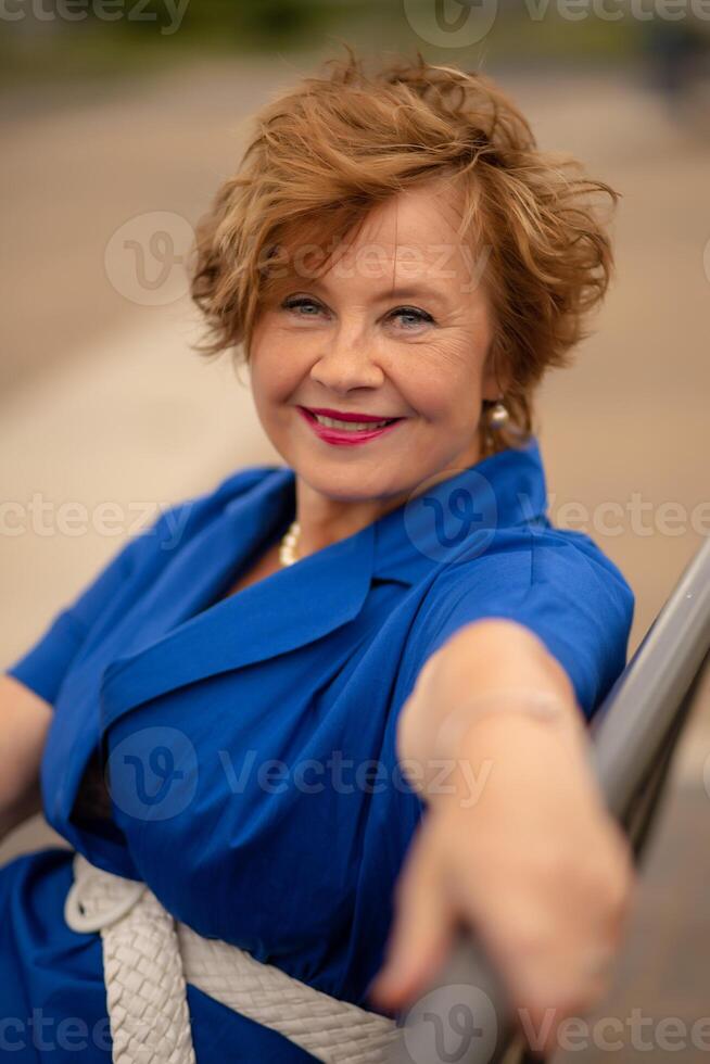 Woman in a blue dress enjoying a sunny day while sitting on a railing at a park photo