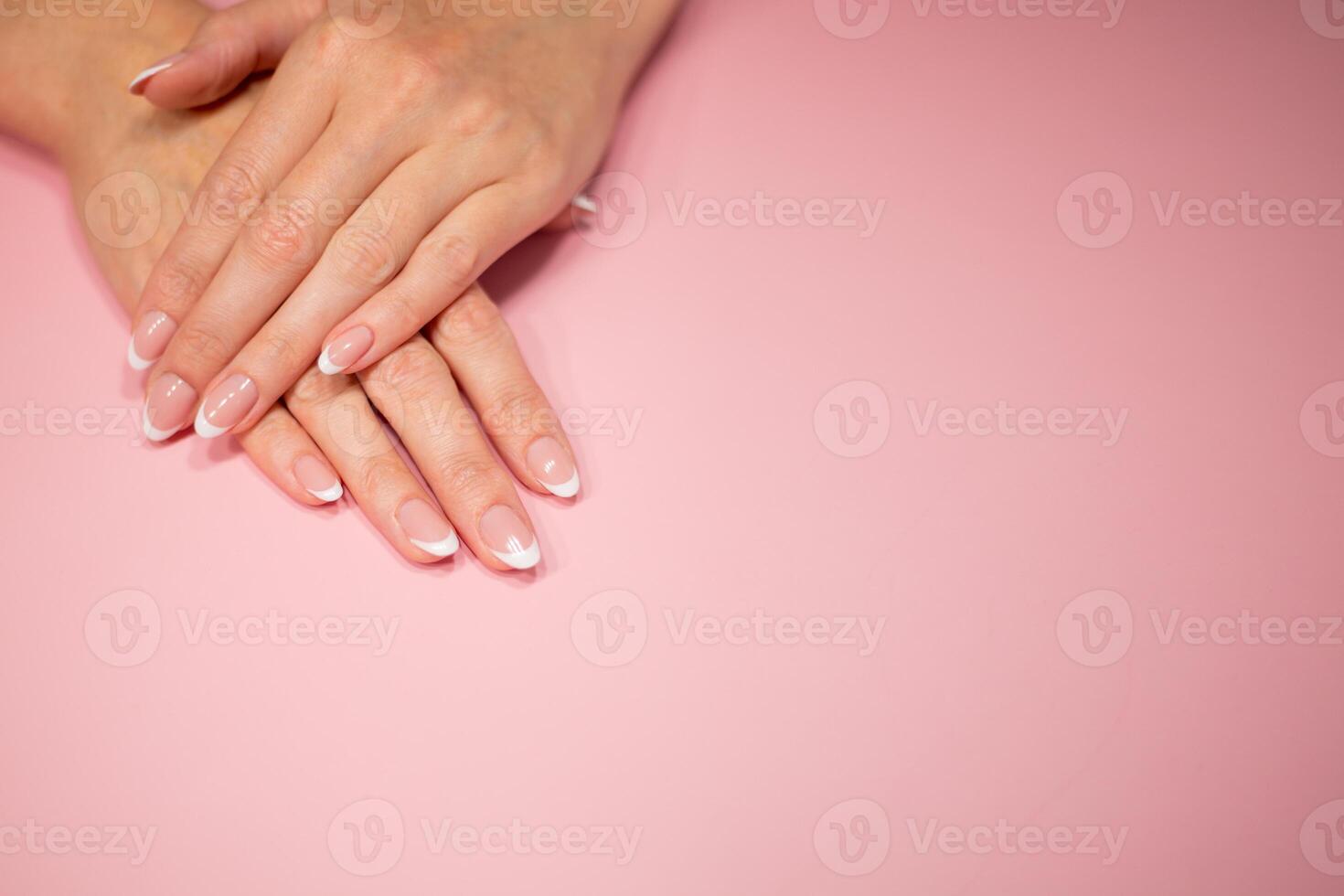 female hands with beautiful classic french white manicure. Fingers isolated on a pastel pink background photo