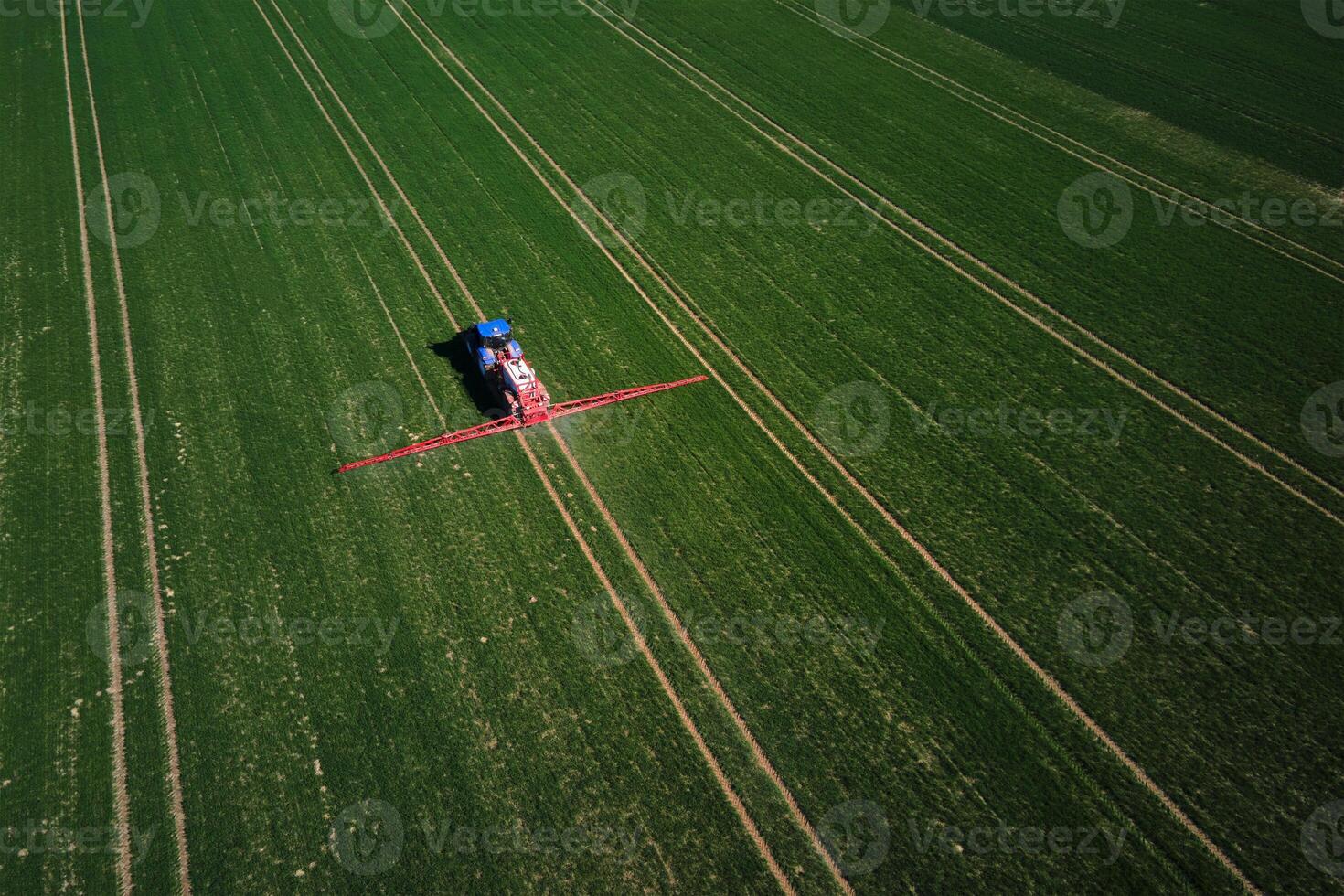 Tractor working in agricultural field, aerial view. Tractor spraying crop field with fertilize or pesticide for good harvest. Concept of farming technology and crop care photo