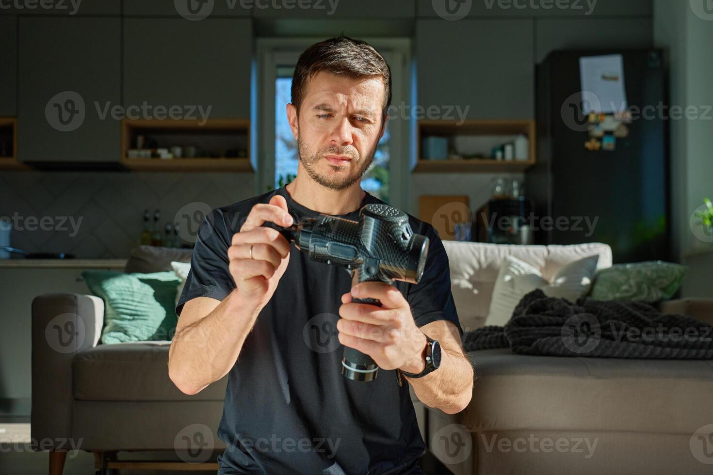 Close-up of man holding massage gun and pressing its vibrating head against his hand to test its strength and performance. Concept of sports recovery, self-care, and muscle treatment tools photo