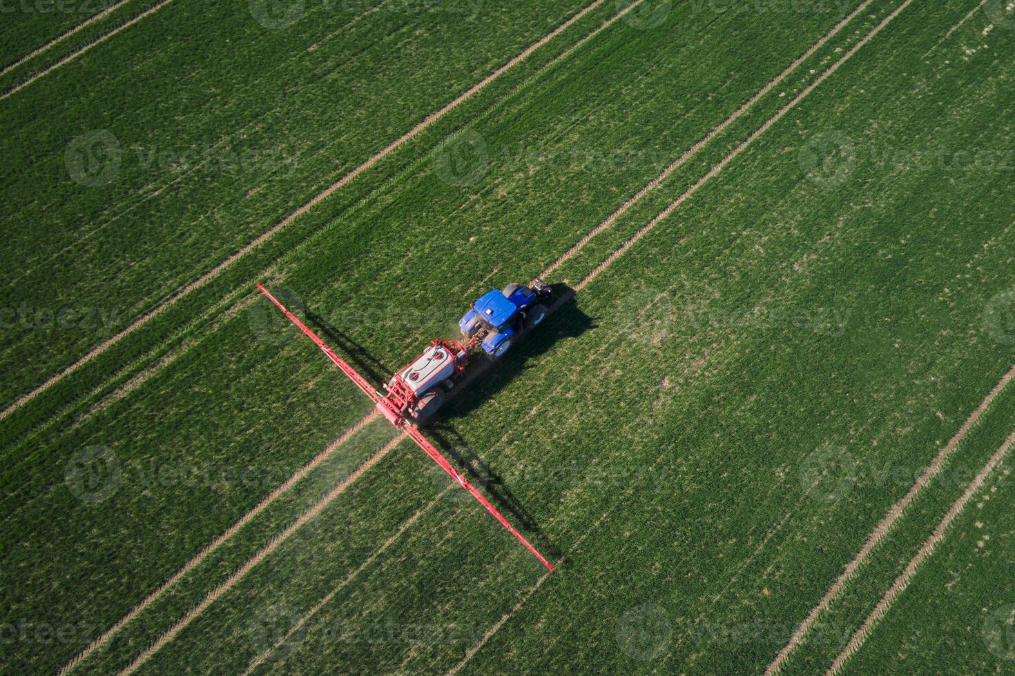Blue tractor working in agricultural field, aerial view. Tractor spraying crop field with fertilize or pesticide for good harvest photo