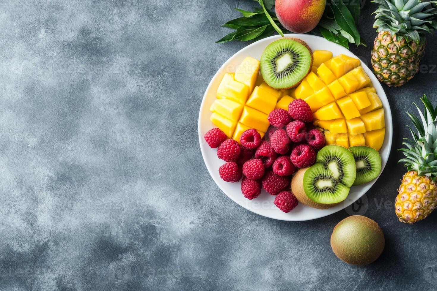 Fresh fruit platter with mango, kiwi, raspberries, and pineapple arranged on a white plate against a textured background photo