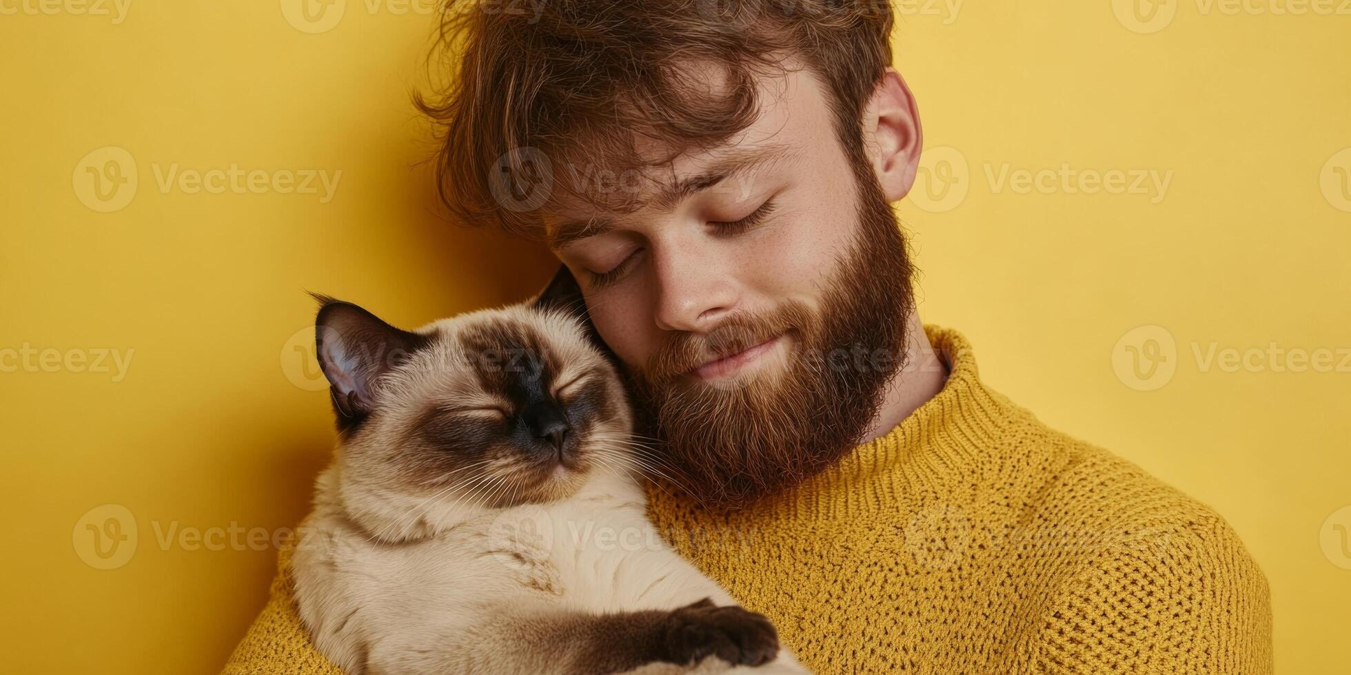 Young man enjoys a joyful moment with his content cat against a vibrant yellow background photo