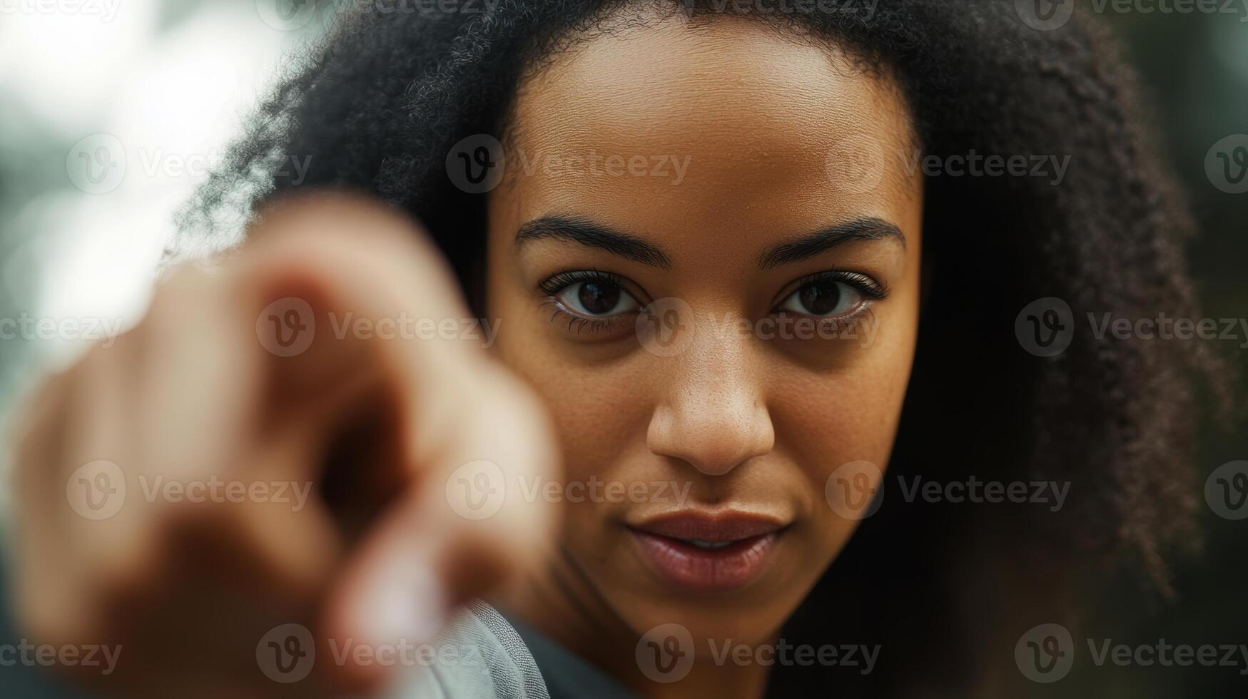 Confident young woman with curly hair pointing directly at the camera in an outdoor setting photo