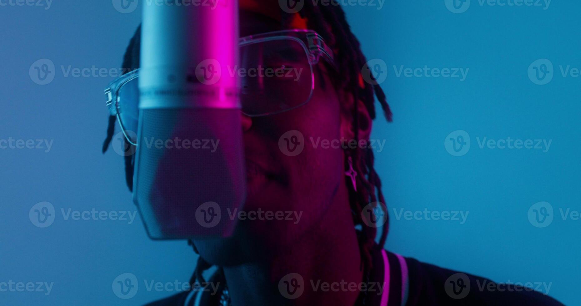 A man with dreadlocks and glasses is in front of a microphone photo
