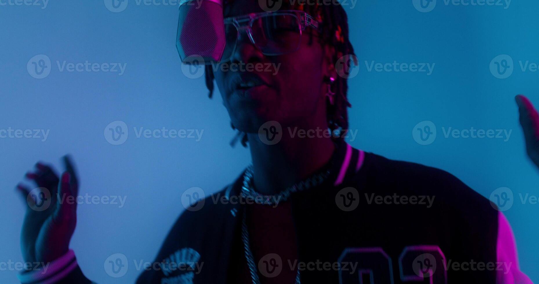 A man with glasses and a black jacket is standing in front of a blue light photo