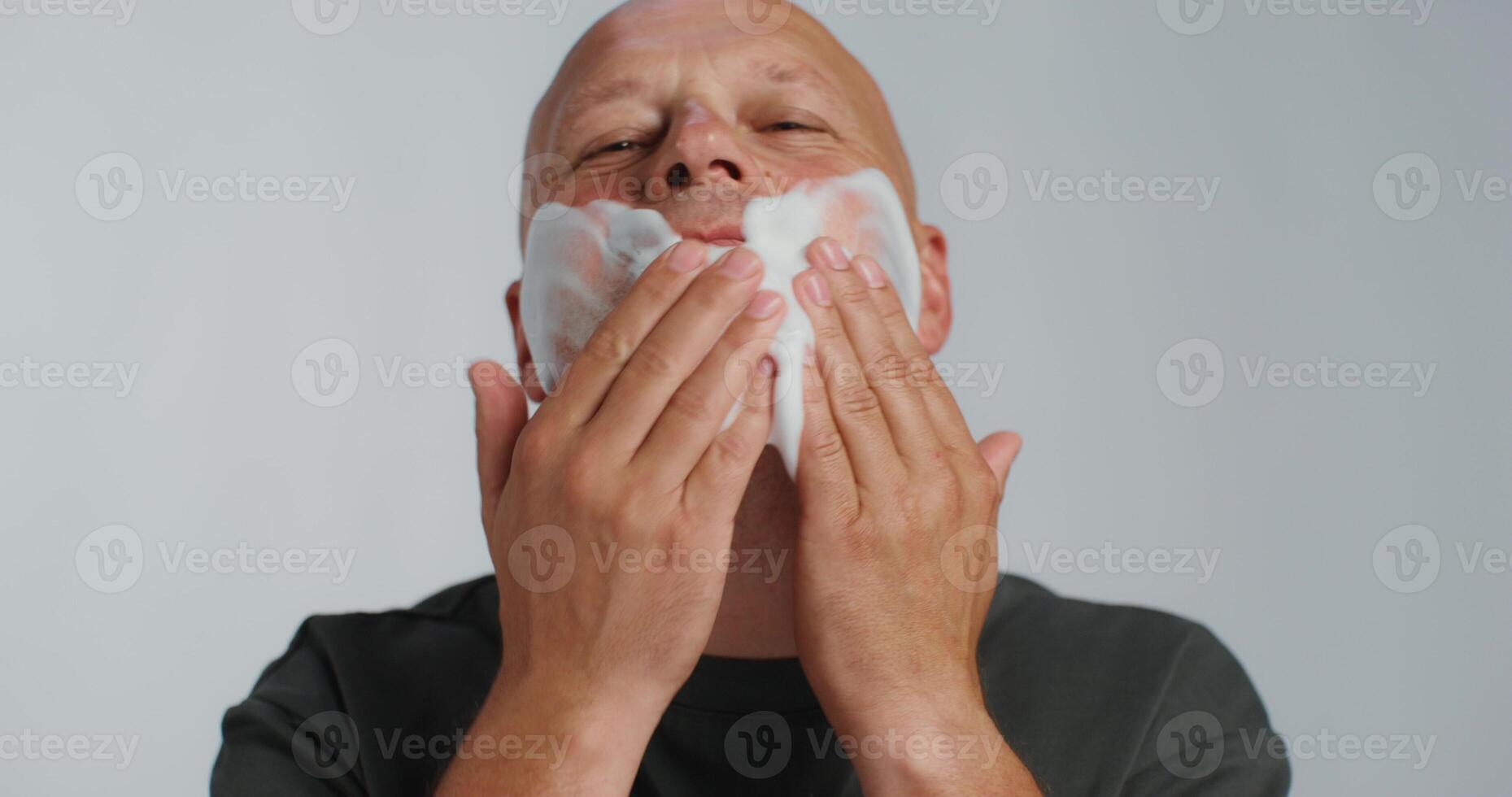 A bald man shaving his face with a razor photo