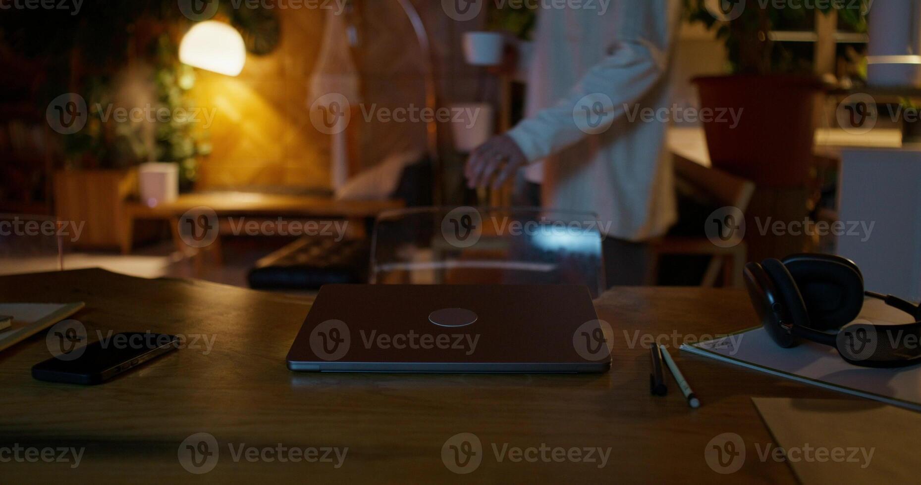 A laptop sitting on a wooden table with a person standing in the background photo
