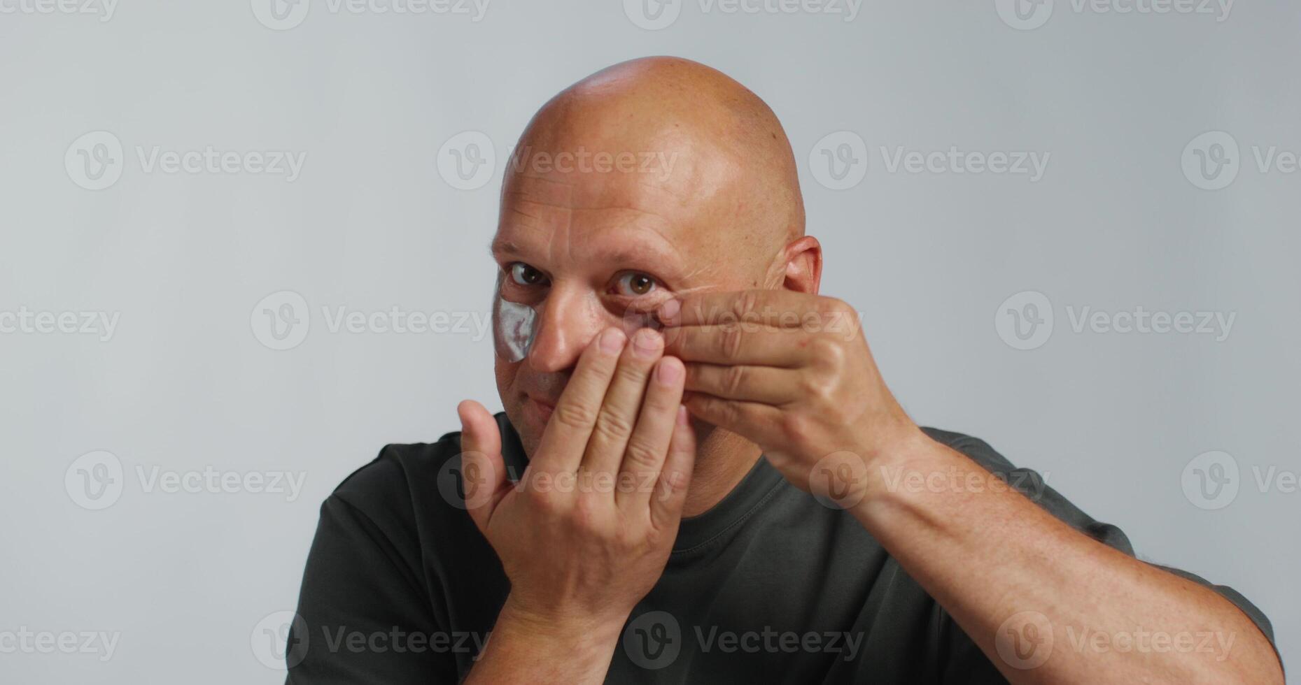 A bald man putting a cream on his face photo