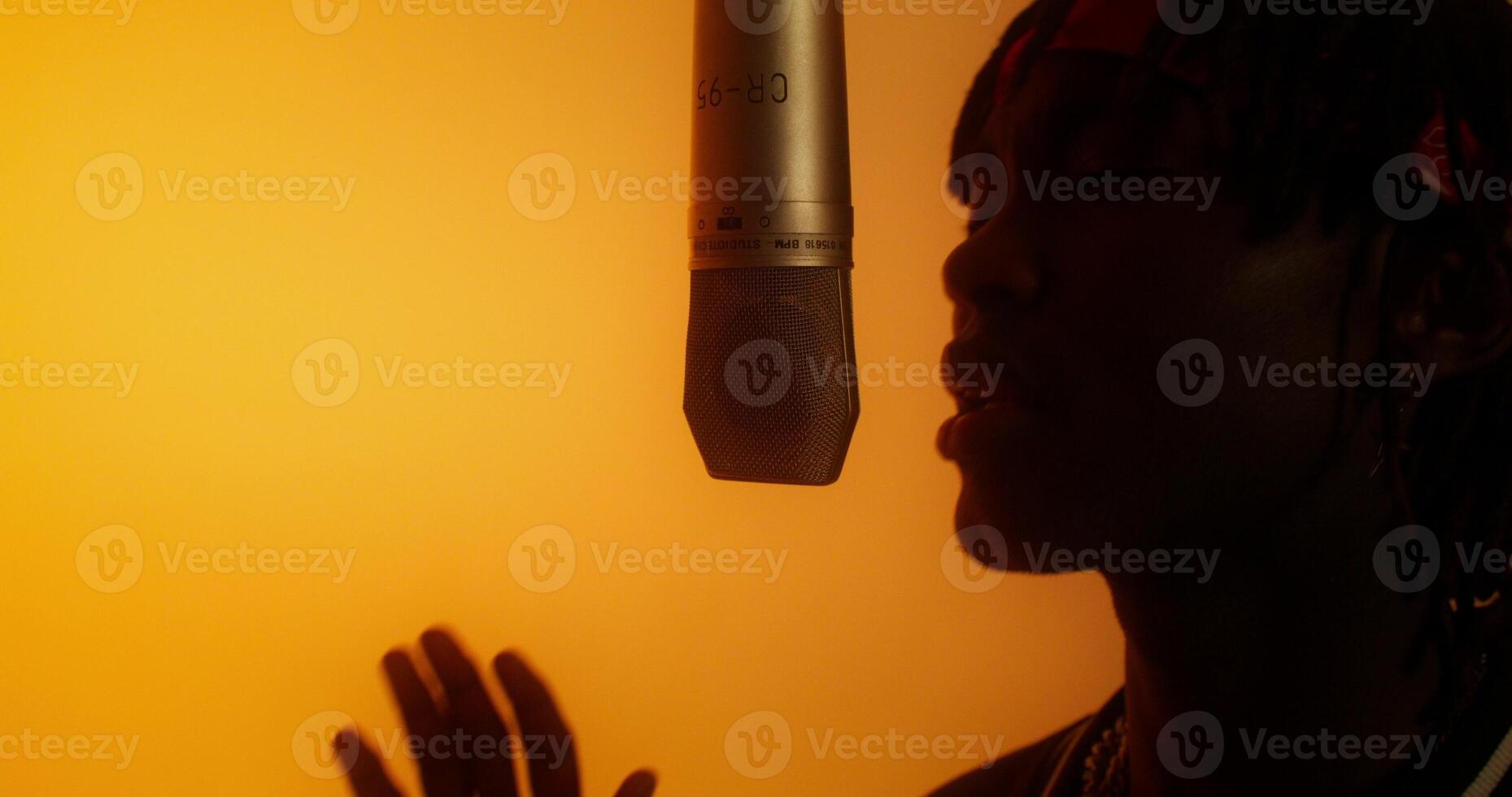 A person singing into a microphone in front of an orange background photo
