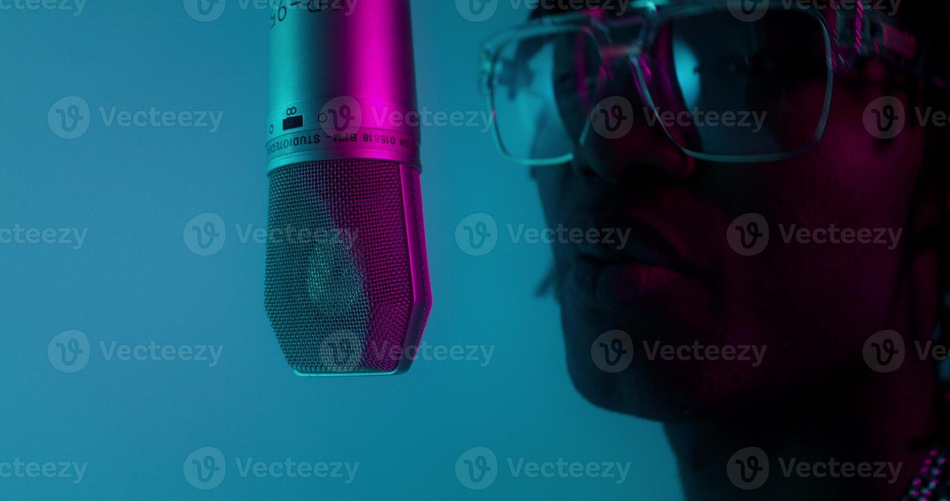 A man with glasses and a microphone in front of a blue background photo