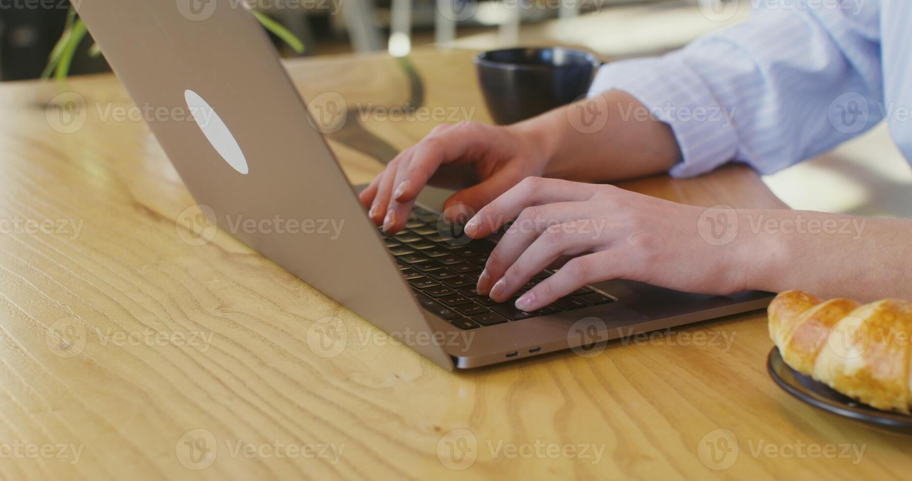 Hands of a fair-skinned woman typing on a laptop sitting at a table in a cafe photo