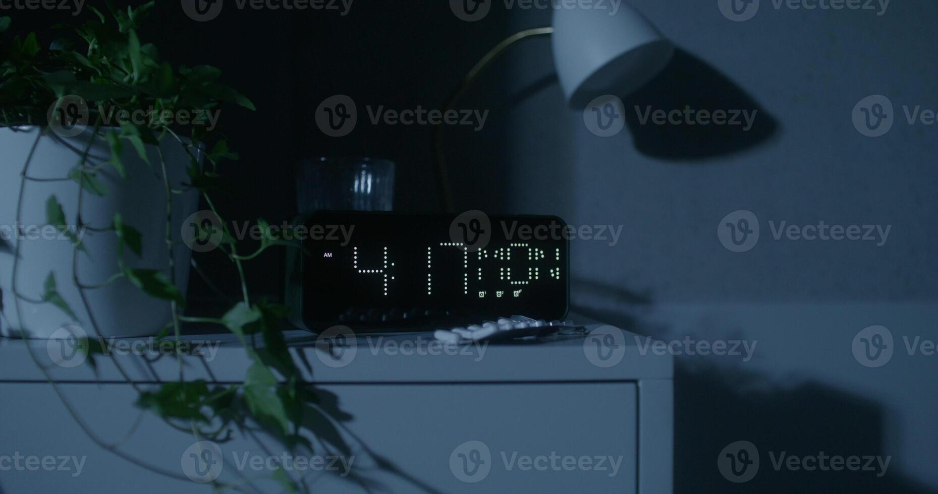A clock is shown on a table in the dark photo