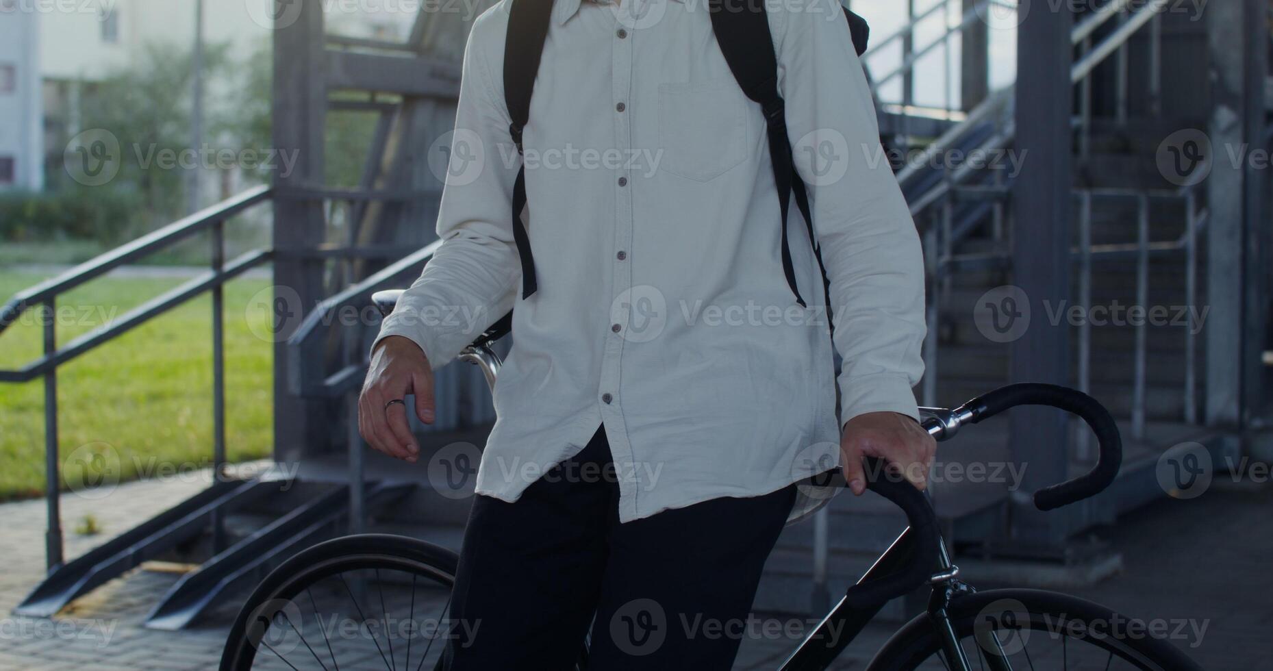 A young man is looking seriously at the camera, leaning on a bicycle photo