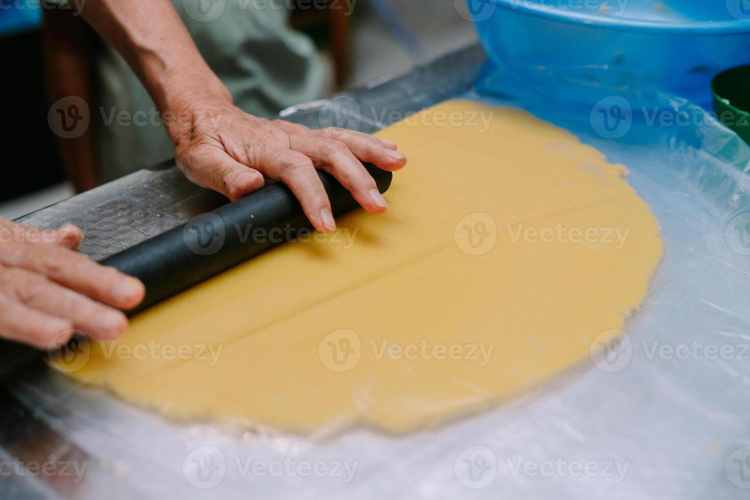 Senior hands rolling yellow dough with rolling pin on a plastic wrap photo