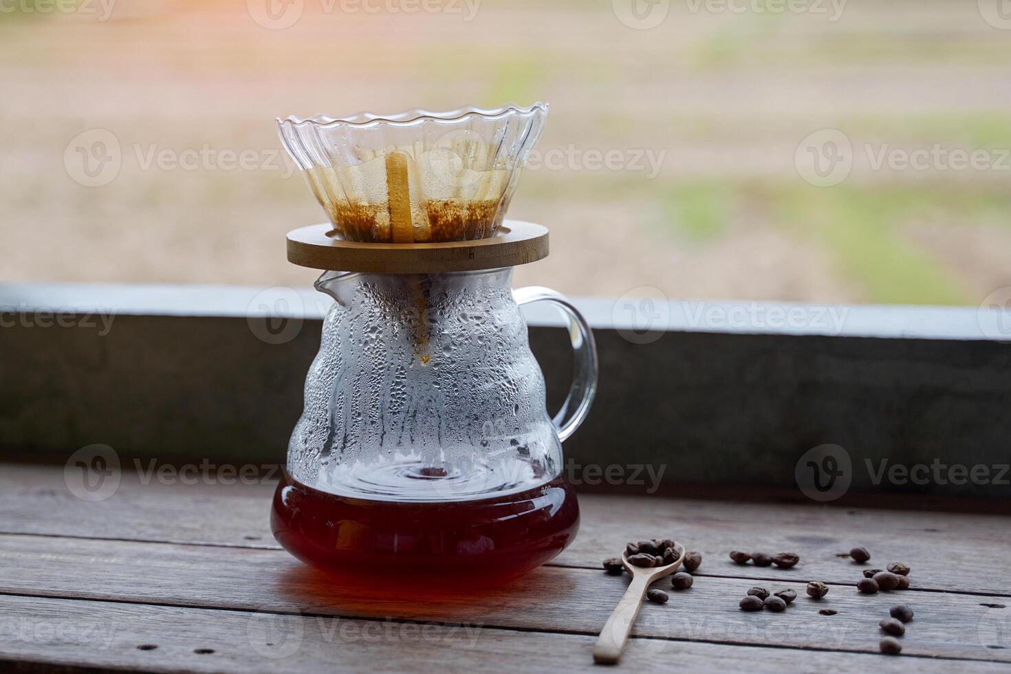 Black coffee in a glass pitcher of a coffee dripper set placed on a wooden counter. photo