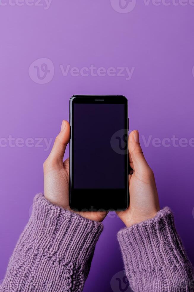 Hands holding a black smartphone against a vibrant purple background in a cozy indoor setting photo