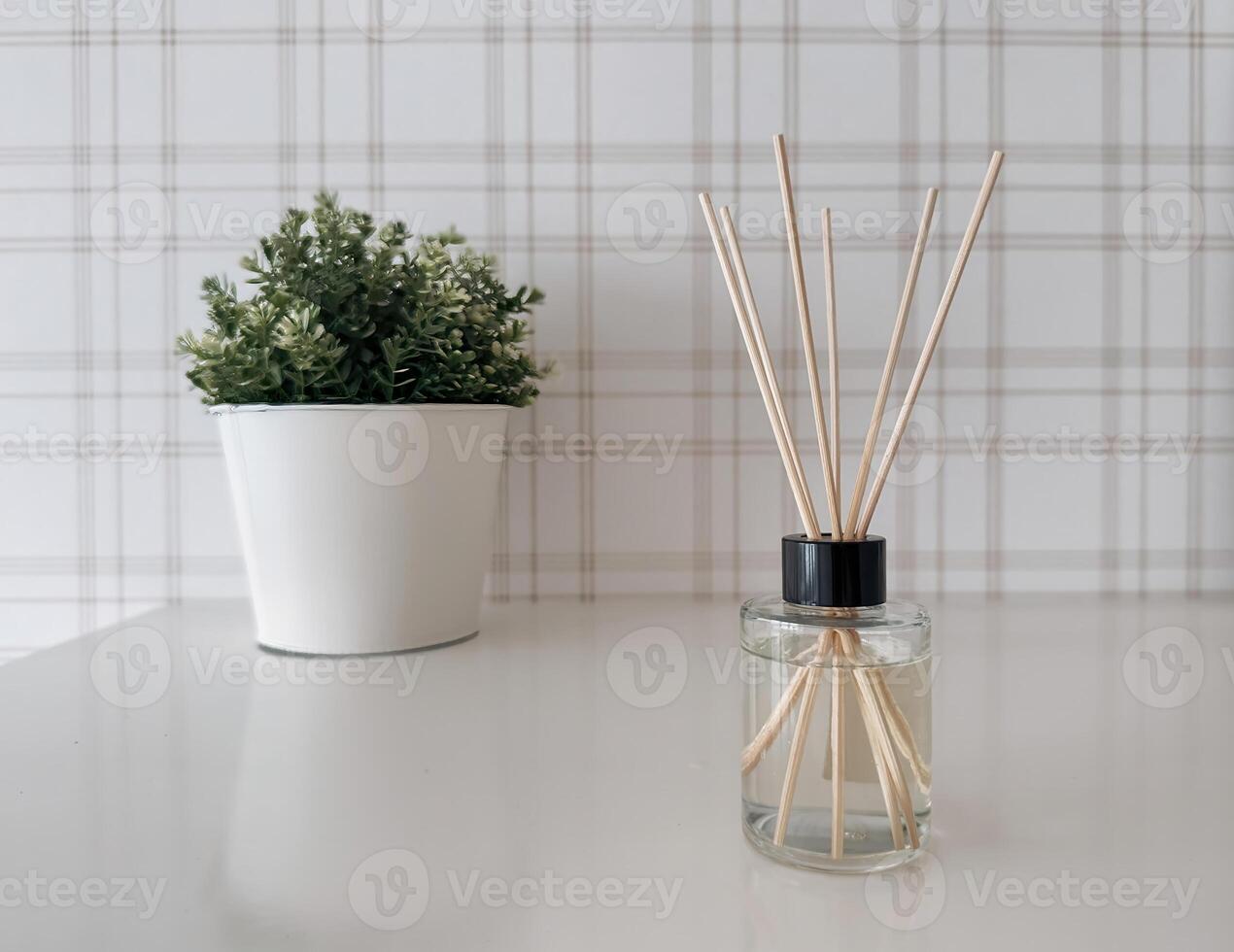 A minimalist home decor scene featuring a white table with a small potted green plant and a glass reed diffuser photo