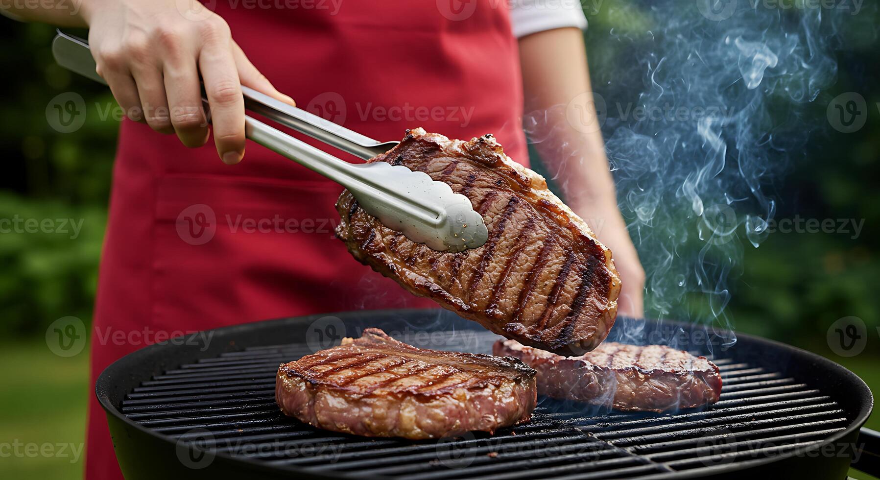 Grilling Delicious Steaks on Barbecue Grill with Smoke and Red Apron photo