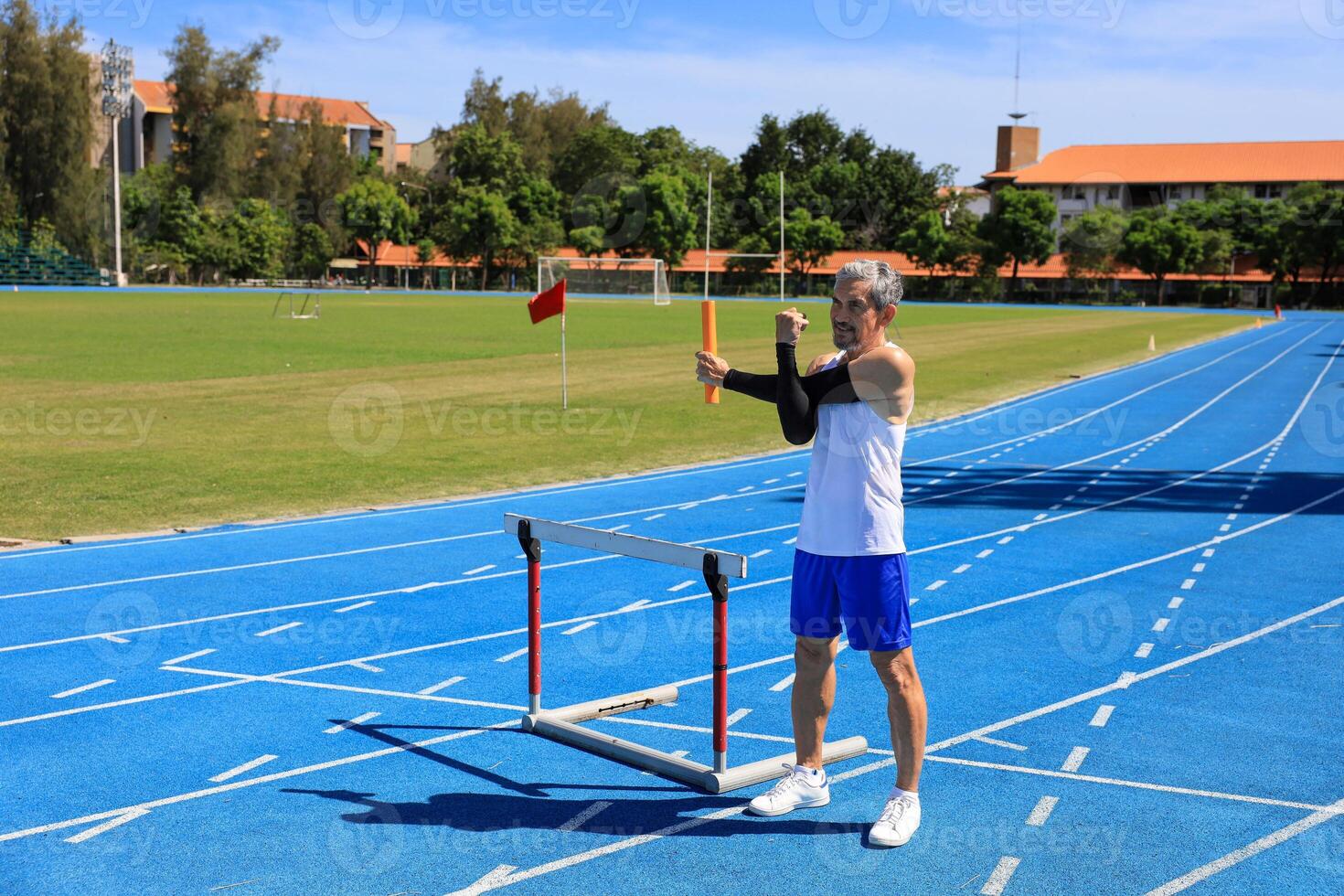Asian senior athlete is practicing hurdling running in the professional blue track for professional exercise, sport training workout and healthy for longevity concept photo