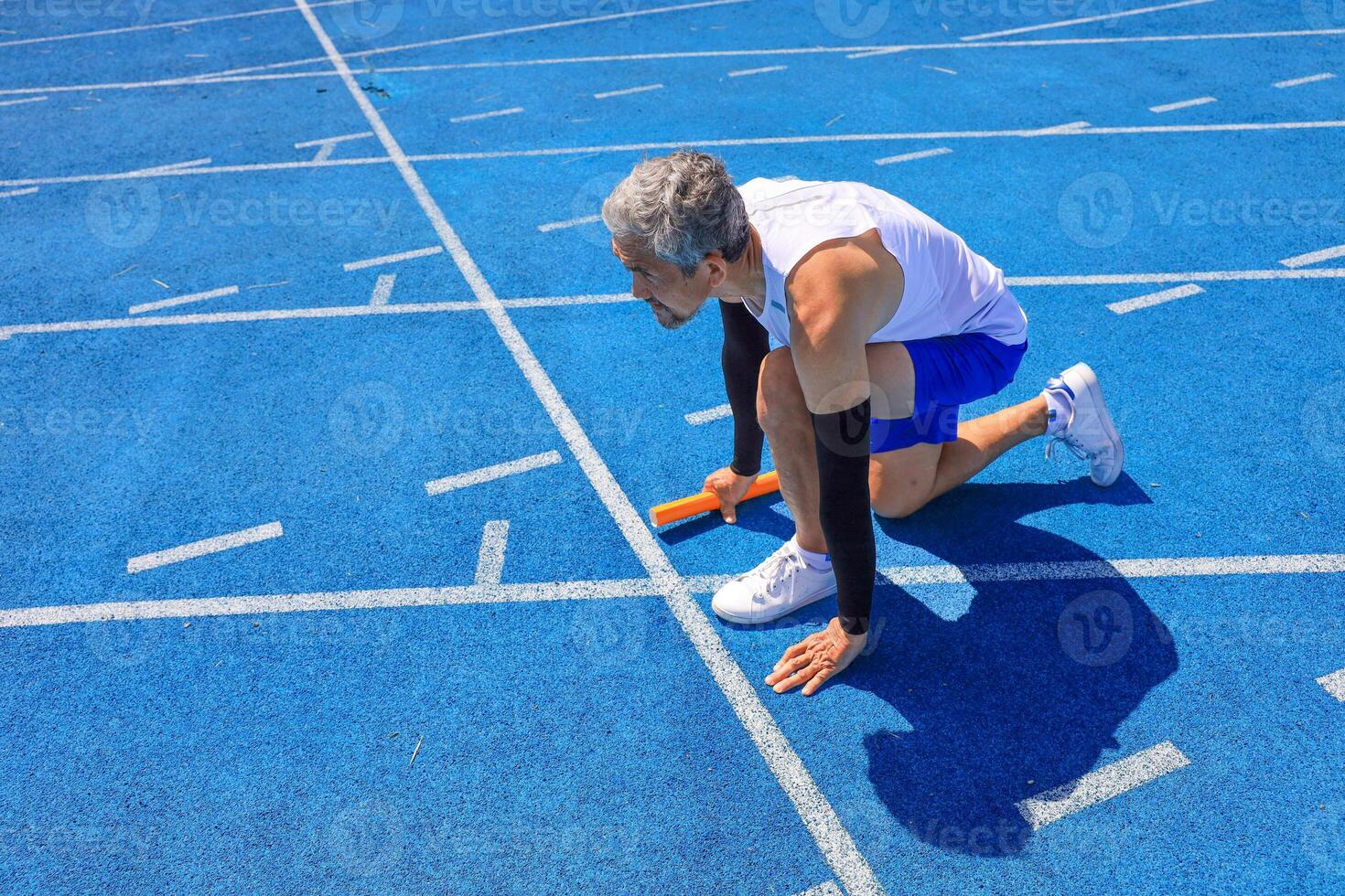 Asian senior athlete is practicing running block start in the professional blue track for professional exercise, sport training workout and healthy for longevity photo