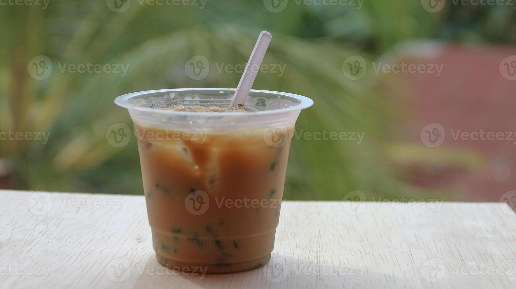 A cup of traditional indonesian iced drink green cendol with brown sugar and coconut milk with a spoon on a wooden table. photo