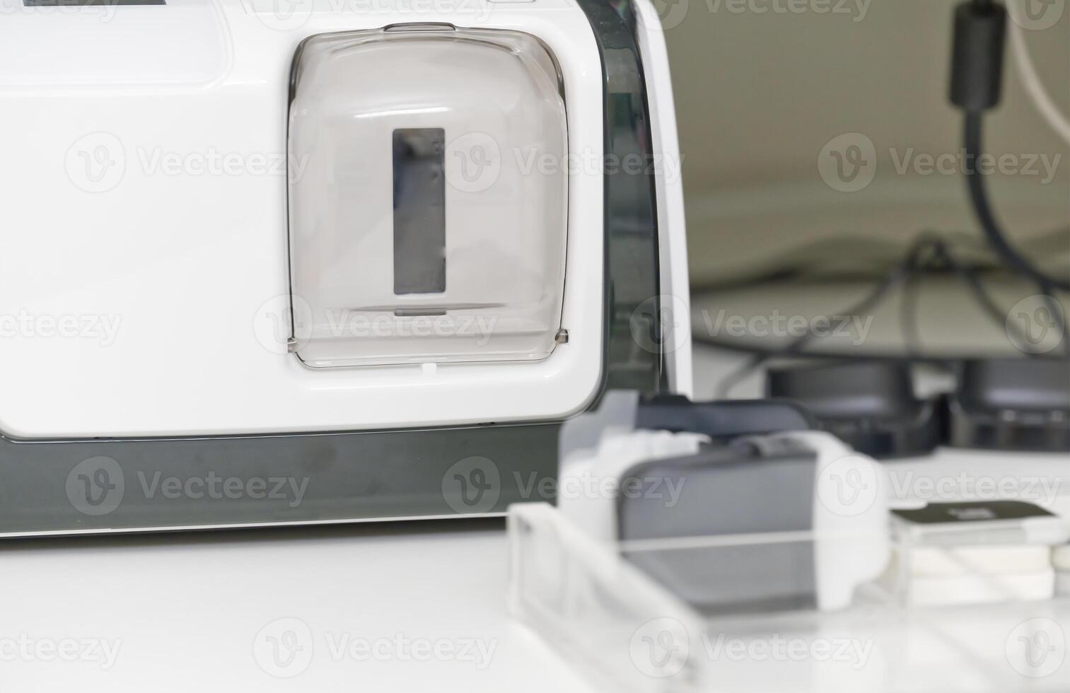 A close-up view of a medical xray scanner with a transparent chamber and various attachments. The background features cables and other equipment, suggesting a clinical setting. photo
